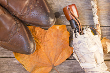 brown shoes, an umbrella and leaves on wooden background.Autumn background