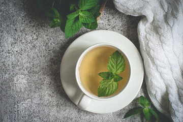 cup of mint tea closeup, fresh mint leaves and a rug on a gray background