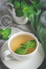 Natural mint tea and fresh mint leaves on a gray background