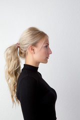 Zufriedene junge Frau mit blonden langen wehenden Haaren im schwarzen engen Pullover vor einer...