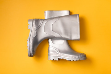 Top view of trendy silver rain boots on orange background.