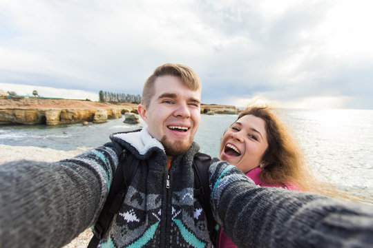 Happy young couple in love takes selfie portrait on the beach in Cyprus in autumn or winter. Pretty tourists make funny photos for travel blog in Europe.