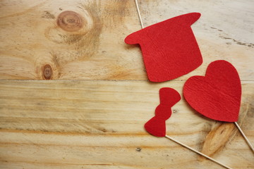 Top or flat lay view of Photo booth props a red heart shape, a red bow tie and a red hat on a wooden background flat lay. Birthday parties and weddings.