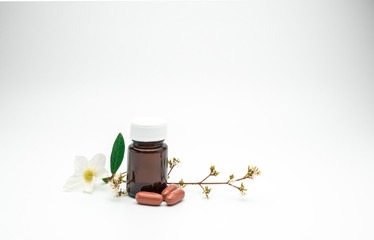 Three orange vitamin and supplement capsule pills with flower and branch and blank label amber glass bottle on white background with copy space, just add your own text