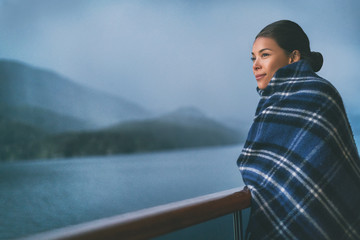 Cruise ship passenger on Alaska travel vacation enjoying scenery at dusk on suite balcony deck with wool throw in cold weather. Asian tourist woman relaxing on summer holiday cruising adventure. © Maridav