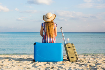 Back view of eautiful young lady with a blue suitcase on the beach. People, travel, vacation and summer concept