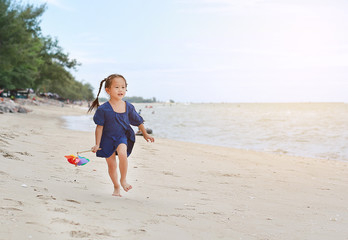 Baby girl hold colorful windmill toy and running on the beach in the evening.