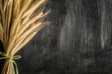 Dried ears of wheat on the dark wooden table. Rustic atmosphere. Harvest background. Top view. - obrazy, fototapety, plakaty