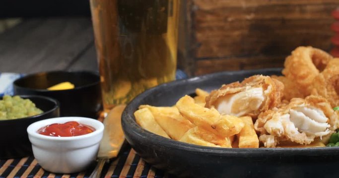 Dolly close up view of an English fish and chips with garden peas, ring onions and mushy peas