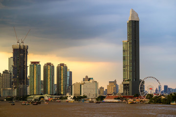 Obraz premium Bangkok skyline cityscape. Buildings, river and boat transportation, ferris wheel at twilight with rain storm and dark cloud and red sky