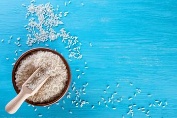 Clay bowl with rice and wooden spatula on blue background