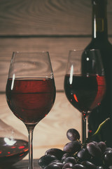 Two glasses and a bottle of red wine and grapes on the table