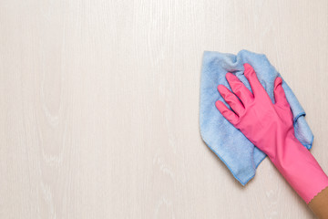 Woman's hand in rubber protective glove wiping white wooden wall from dust with dry microfiber cloth. Early spring cleaning or regular clean up. Maid cleans house.