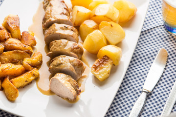 Carn di maiale arrosto con patate e spicchi di mela arrostite servite su un piatto