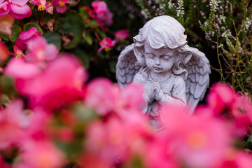 betender Engel kniet zwischen Blumen auf einem Grab auf einem Friedhof