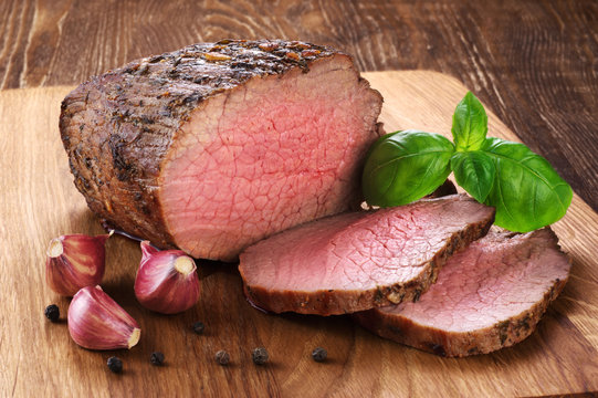Baked meat, garlic and basil on a wooden background. Roast beef.