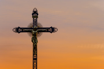 großes Metallkreuz mit Jesus im orangen Sonnenuntergang