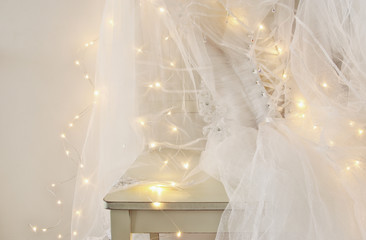 Beautiful white wedding dress and veil on chair with gold garland lights
