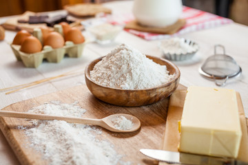 Baking ingredients in rural kitchen - dough recipe ingredients (eggs, flour, milk, butter, sugar) and rolling pin on wooden white table.