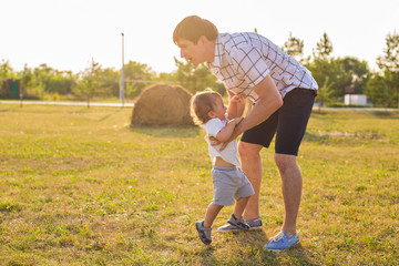Happy young father and son playing together and having fun in the summer or autumn field. Family, child, fatherhood and nature concept