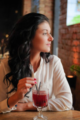 Girl drinks mulled wine in coffee shop.Lovely girl looking out the window in the restaurant and waiting for their friends. Young woman on a date in the cafe. Sexy girl in dreams is sitting in the cafe