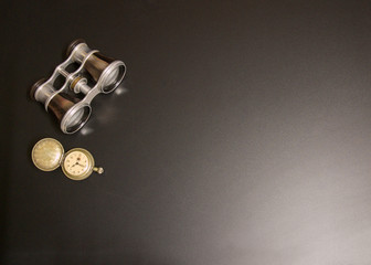 Old vintage binoculars and vintage locket clock style on black background.