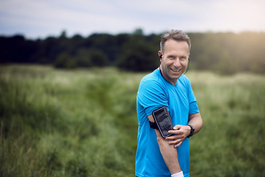 Sportlicher gl&uuml;cklicher Mann stellt zum Sport sein Smartphone ein