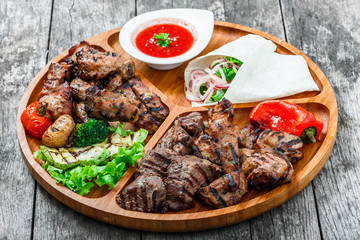 Assorted delicious grilled meat and vegetables with fresh salad and bbq sauce on cutting board on wooden background close up. Hot Meat Dishes. Top view
