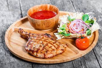 Grilled beef steak on bone, fresh salad, grilled vegetables and tomato sauce on cutting board on wooden background. Hot Meat Dishes