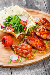 Fried chicken wings with fresh salad, grilled vegetables and bbq sauce on cutting board on wooden background close up. Hot Meat Dishes. Top view