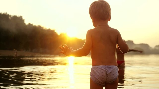Little child stands on the beach during beautiful sunset happy vacation time in slow motion. 1920x1080