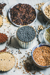 Various raw uncooked grains, beans, cereals in bowls and cups for healthy cooking over marble background, selective focus. Clean eating, dieting, healthy, detox, vegan, vegetarian food concept