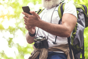 Cheerful mature tourist messaging on phone in nature
