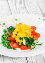 Fresh salad with cherry tomatoes, cucumber, radish, sweet pepper and onion in a plate on wooden background close up. Top view