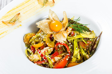 Salad with chicken breast and grilled vegetables, eggplant, sweet pepper, tomatoes, avocado and physalis on plate on wooden background close up. Top view