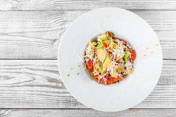 Fresh salad with chicken breast, artichokes, cherry tomatoes, lettuce and cheese parmesan on wooden background close up. Top view