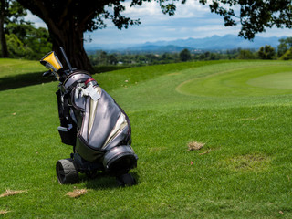 Golf equipments, clubs, driver, fairway wood, irons, putter in golfer's golf bag on green grass fairway in golf course with beautiful landscape and blue sky