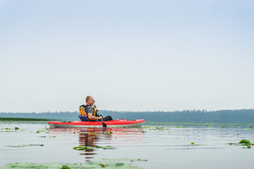 Man paddling kayak among lily flowers on the lake