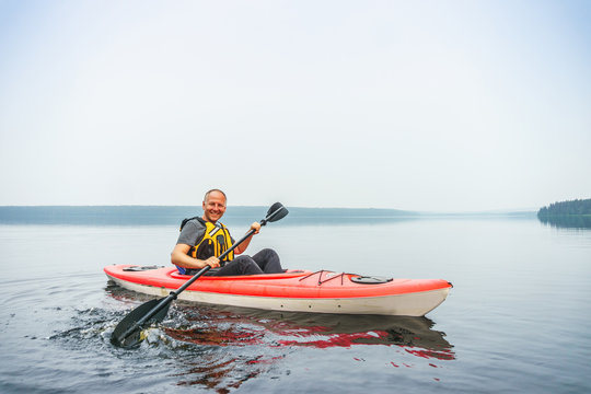 Man paddling in kayak on a calm, misty lake