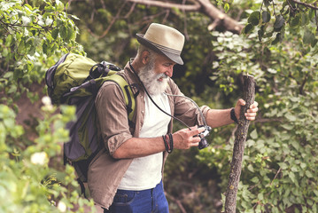 Glad old male tourist looking at photographs of nature