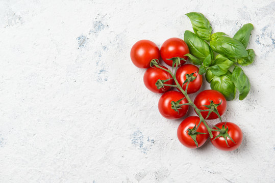 Fresh cherry tomatoes with basil leaves on a stone table, top view with copy space