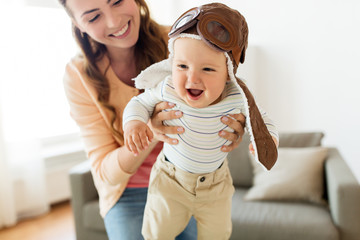 happy mother with baby wearing pilot hat at home