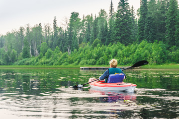 Fototapeta na wymiar Woman in a kayak paddling along the lake shore
