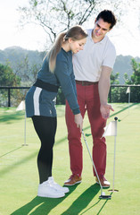Obraz premium Man 30-35 years old is training woman 25-29 years old to play golf