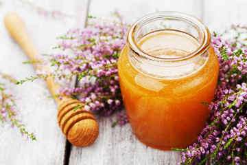 Obraz na płótnie Canvas Golden honey in pot or jar and flowers heather on wooden vintage table.