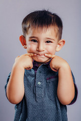 Studio portrait of face of a small funny caucasian boy crummy and stretching his fingers in the mouth in a smile