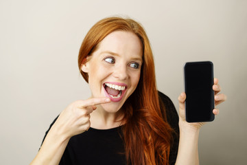 glückliche frau zeigt mit dem finger auf ihr mobiltelefon