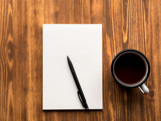 tea Cup, pencil or pen and open Notepad with a clean white page on wooden table, top view
