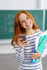 lächelnde junge frau in der schule hält ihr handy in der hand