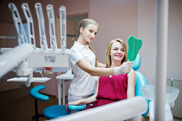 Beautiful dentist showing her patient's new teeth through the mirror in dental cabinet.